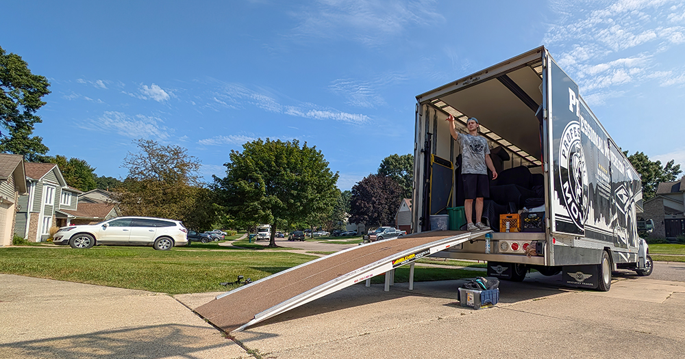 Professional moving truck with ramp in residential neighborhood, showcasing efficient equipment and local moving services by uniformed mover